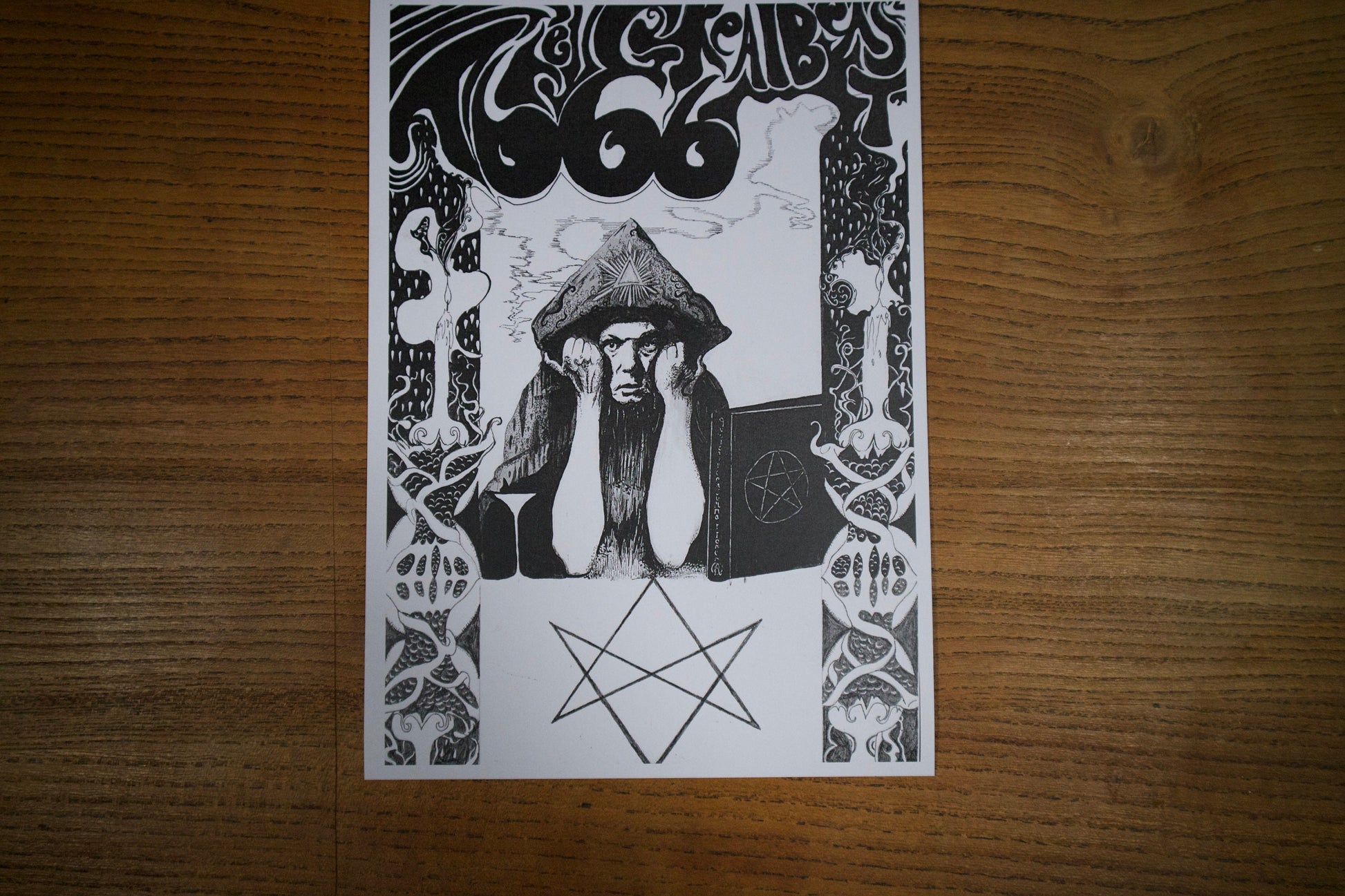 A print on a table of A black and white pen and ink portrait of Aleister Crowley in a psychedelic art nouveau style, the text above reads The Great Beast 666